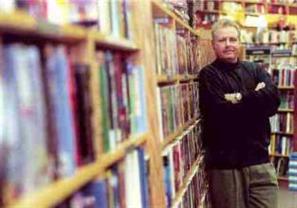 Image: Author John Snyder taking a break from a book signing and leaning against a shelf of books at Borders Books.
